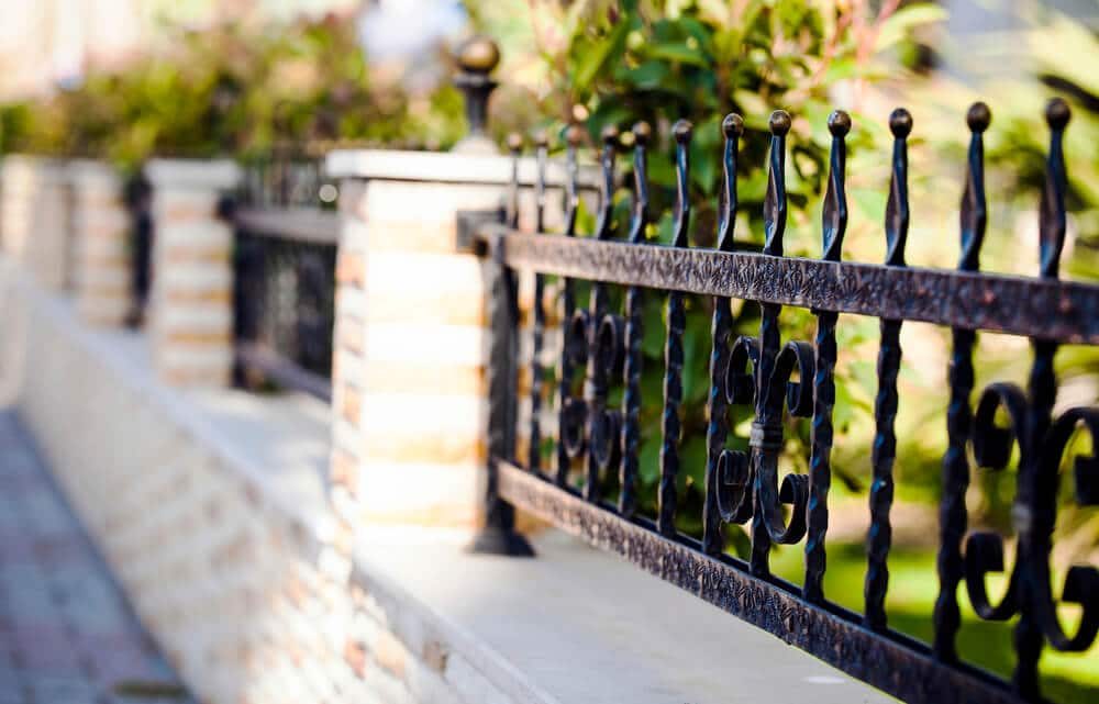 A black wrought iron fence with twisted bars and scrollwork set between brick and stone pillars