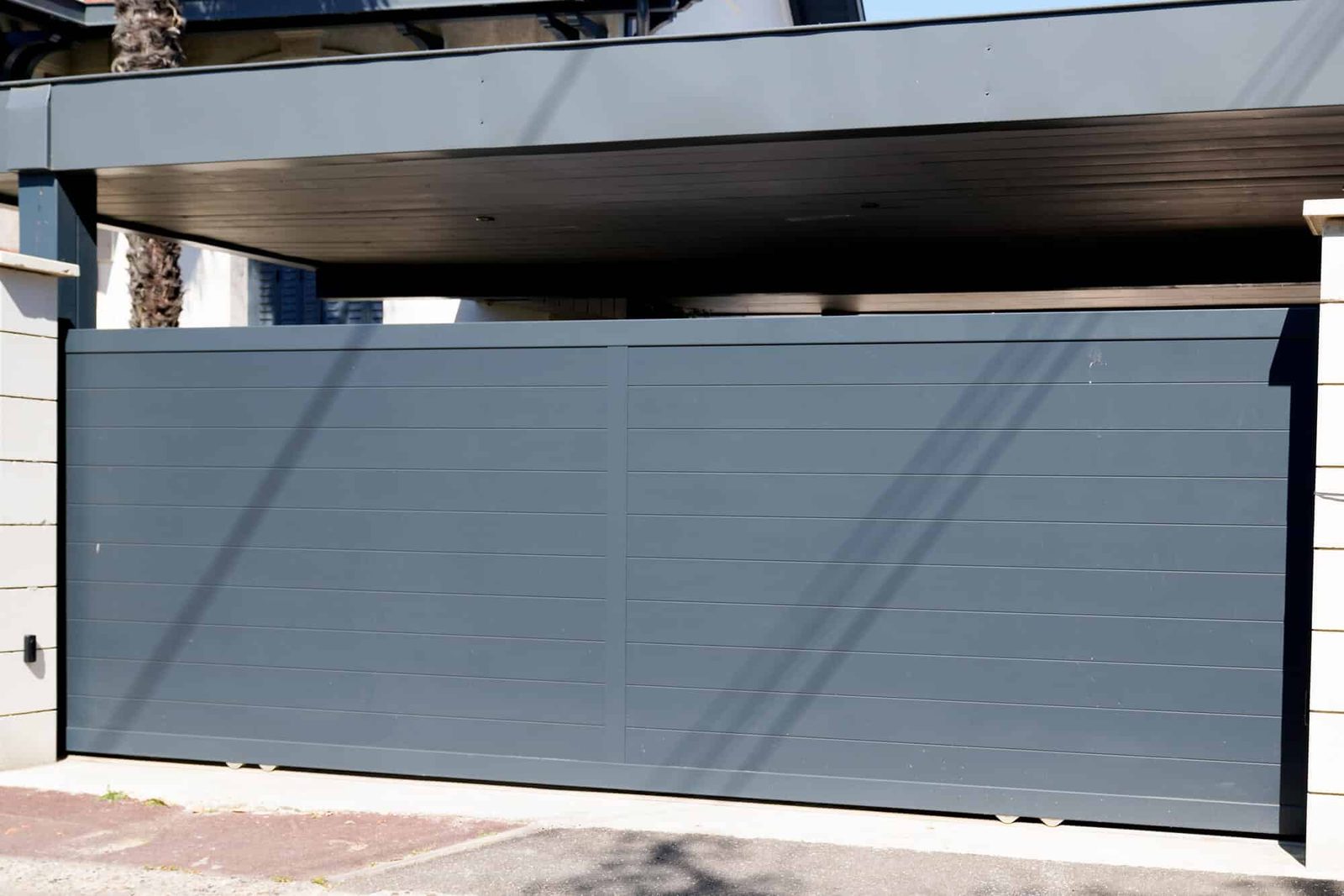 Gray powder-coated aluminum sliding gate between white masonry pillars