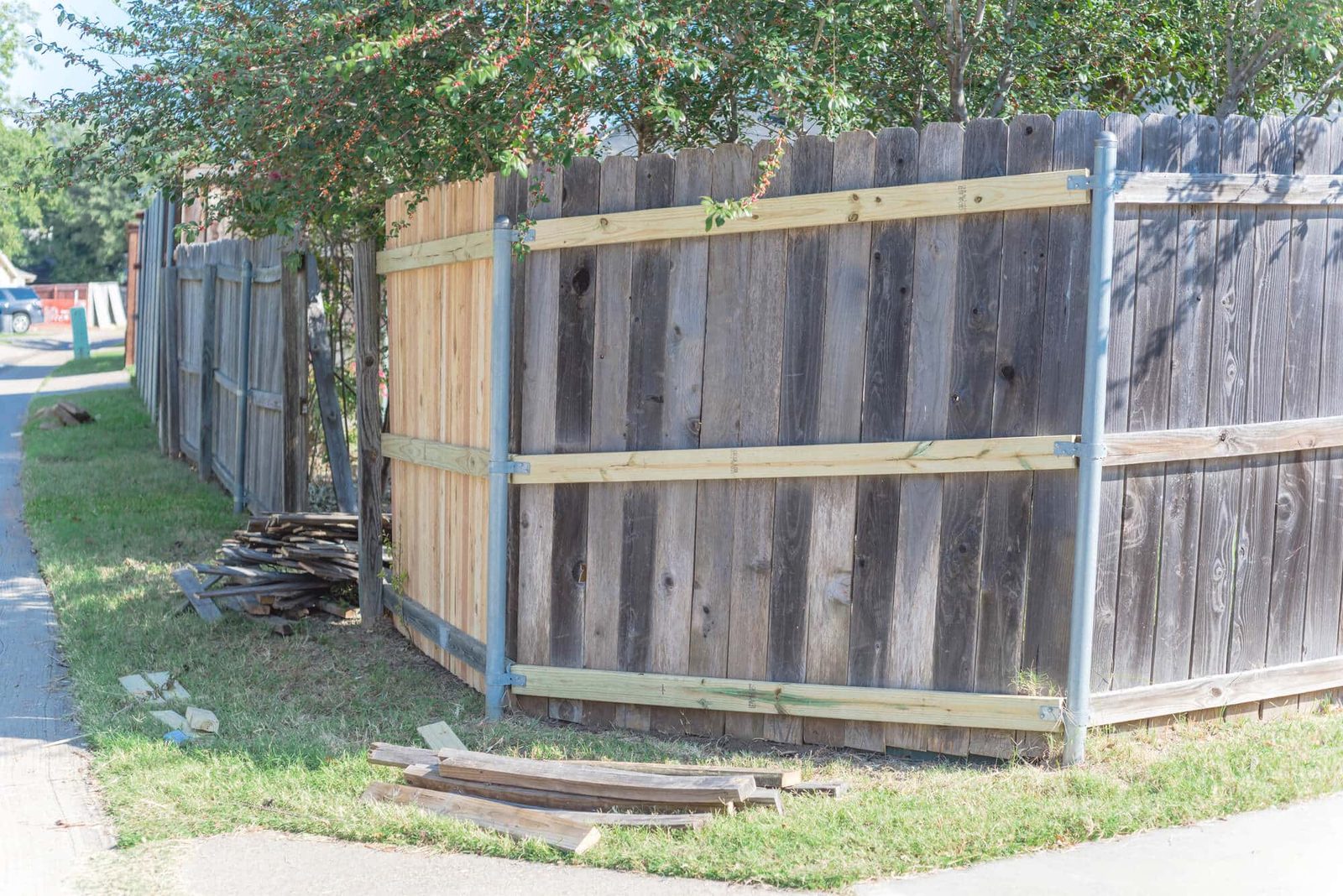 Weathered gray wood privacy fence being repaired with new rails and metal posts