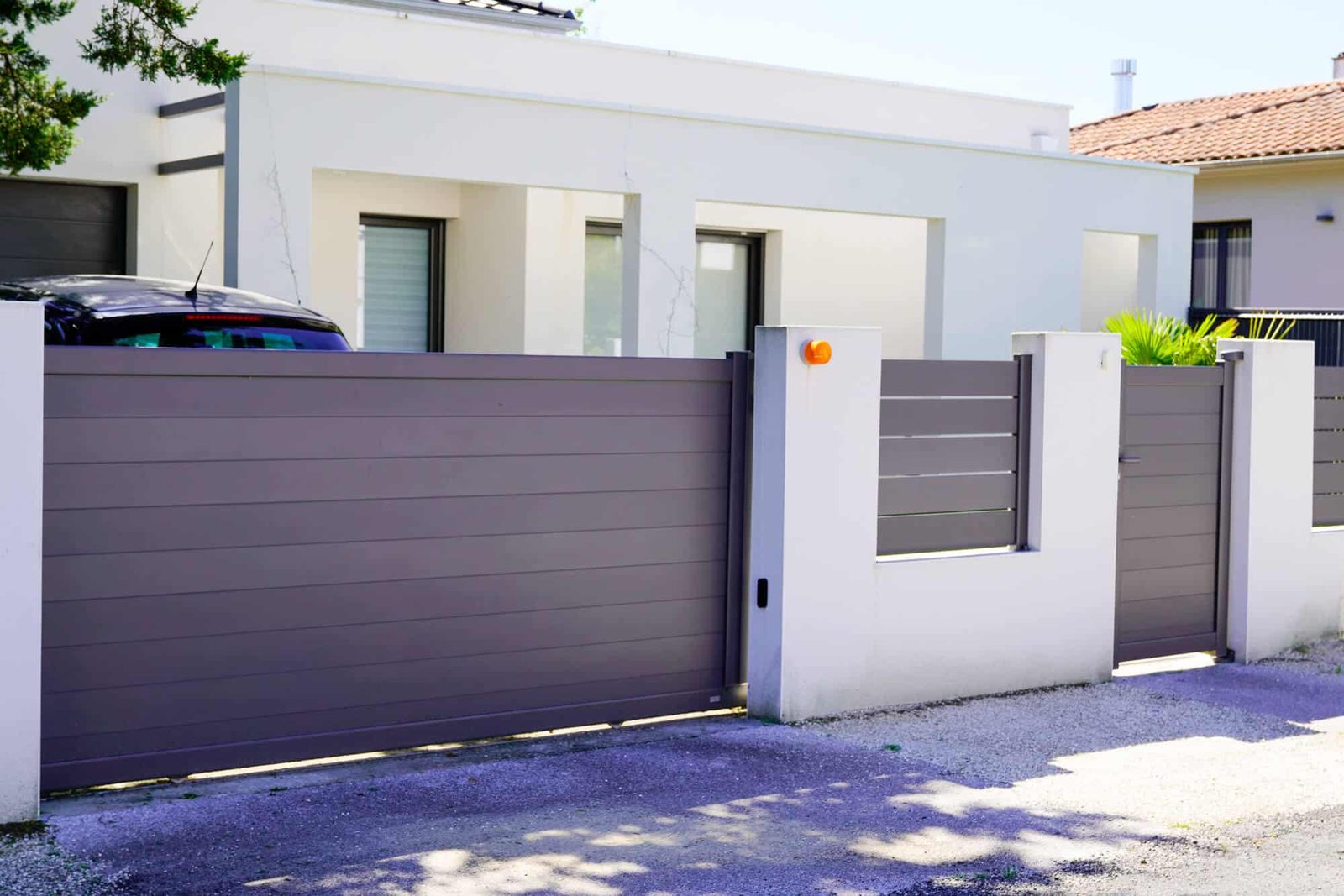 Taupe aluminum sliding gate and matching fence panels set between white masonry pillars
