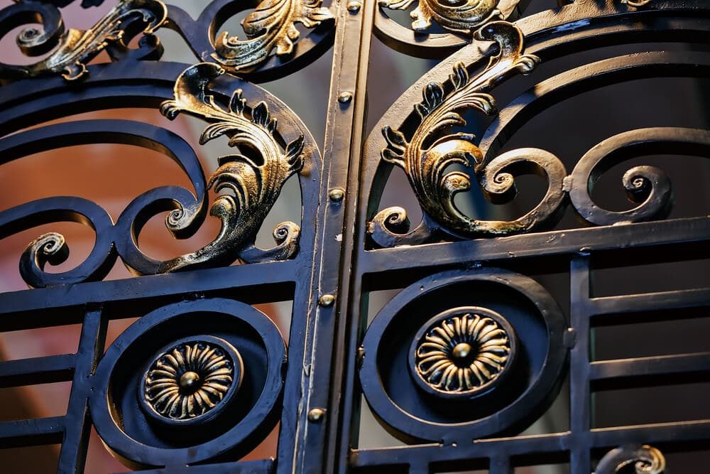 Close-up of a black iron gate with gold-highlighted scrolls and rosettes