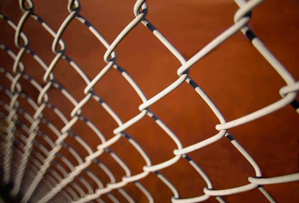 Close-up of a chain link fence with a coated wire mesh against an orange background