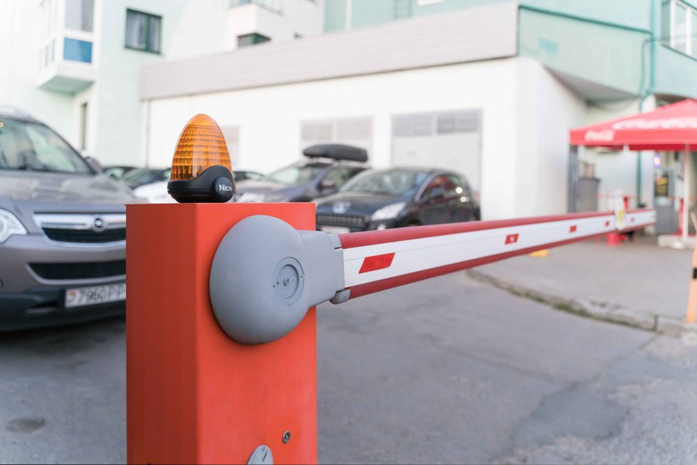 A closed red and white barrier arm gate with an amber warning light, with cars parked behind it