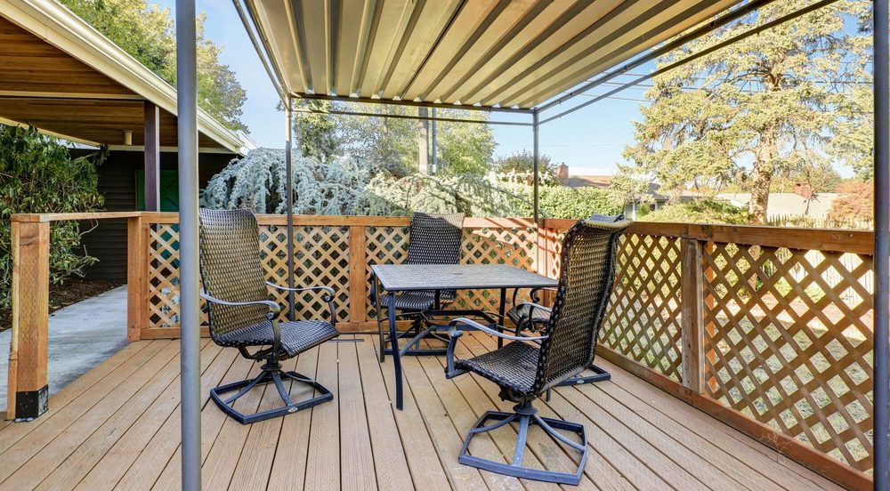 A wood deck with patio chairs and a table under a metal-roofed canopy