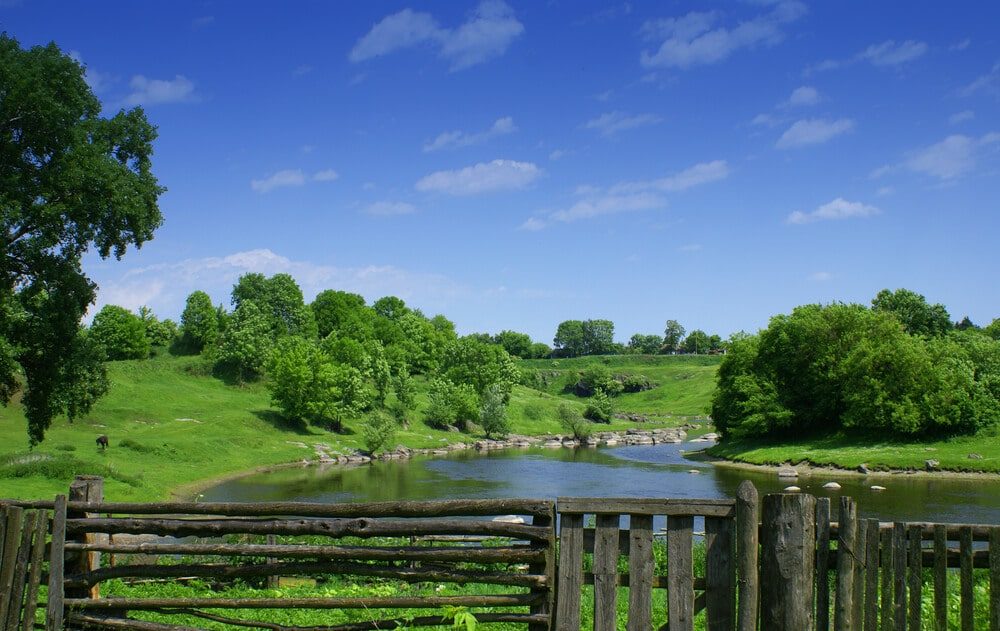 A rustic wood rail fence and board gate overlooking a river and green hills
