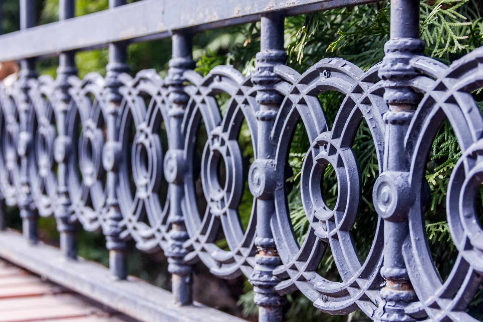 Gray ornamental metal railing with an interlocking circle pattern above green shrubs