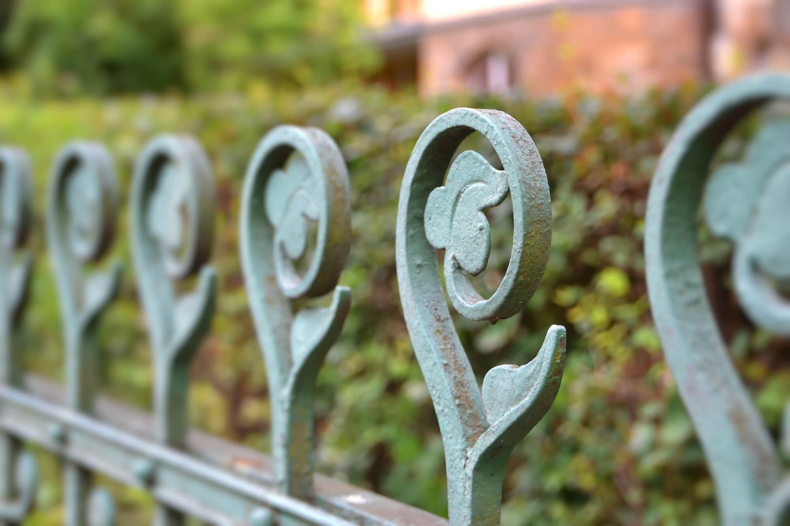 Green scrolled finials on an older iron fence with worn, chipped paint