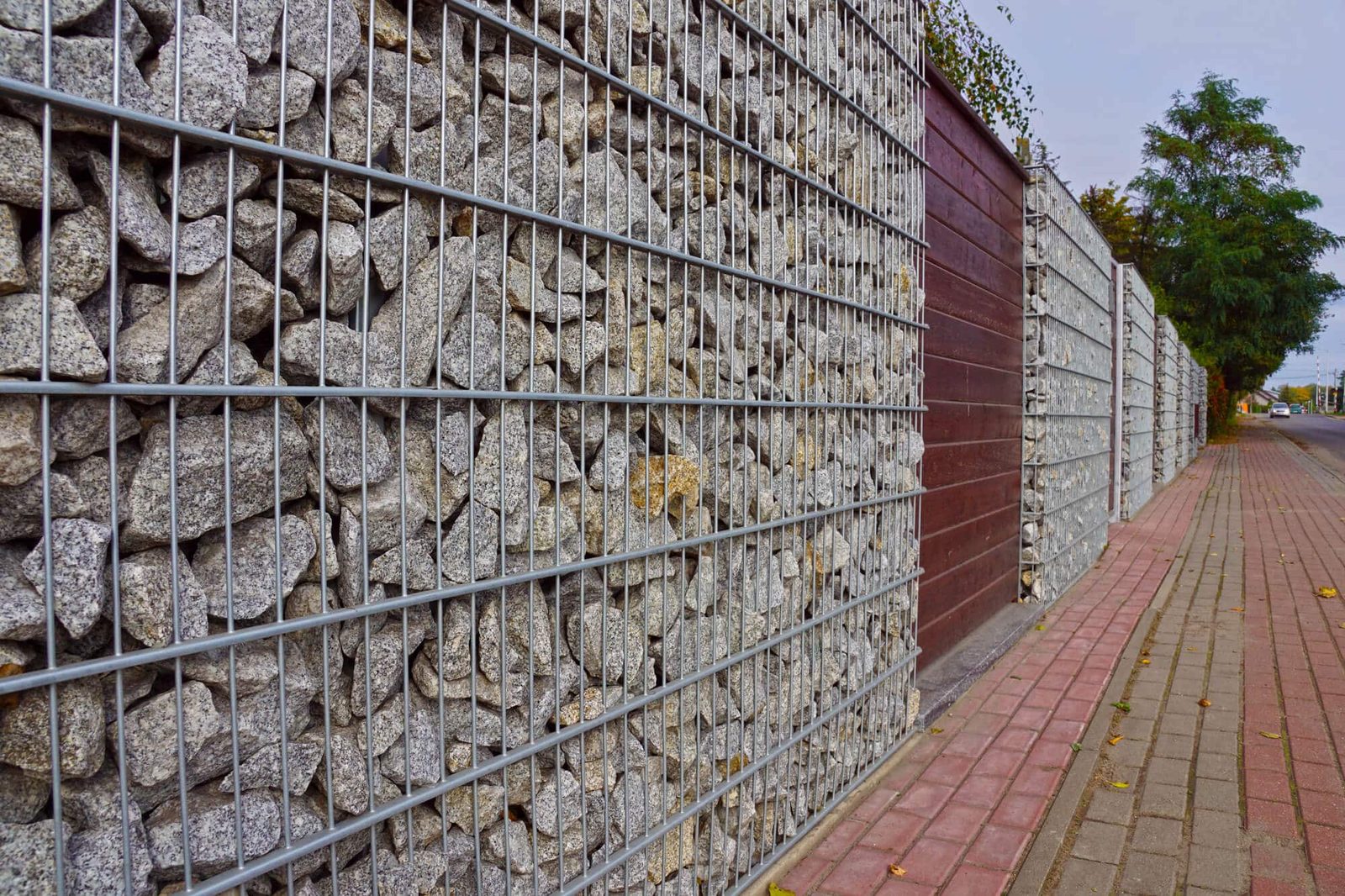 Galvanized welded wire panels filled with granite stones beside a brick sidewalk