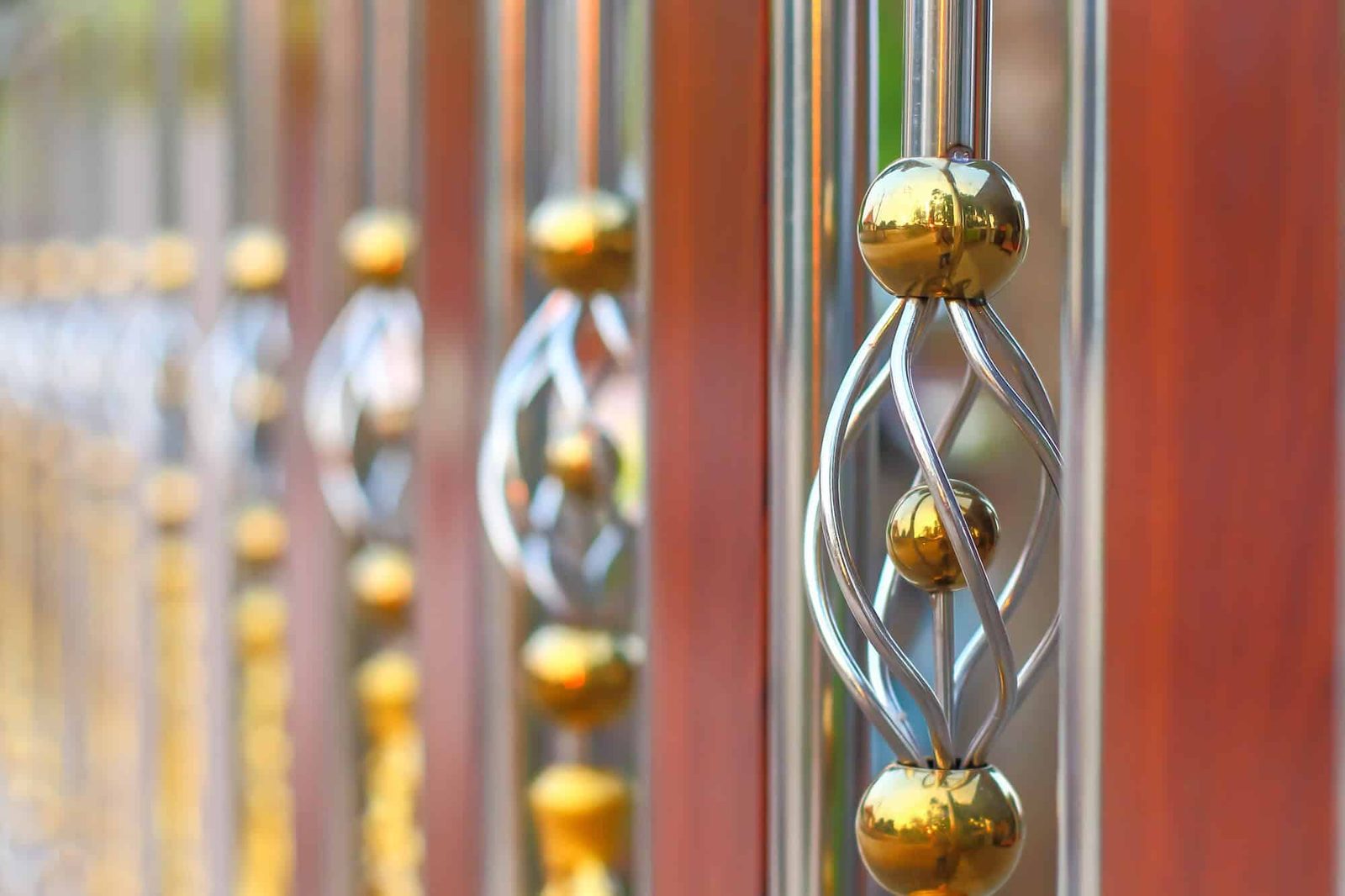 Close-up of polished stainless steel fence bars with twisted cage ornaments and brass-colored balls