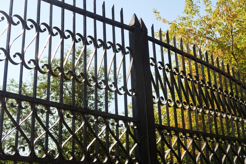 Black wrought iron fence with scrollwork panels and pointed tops against green and gold leaves