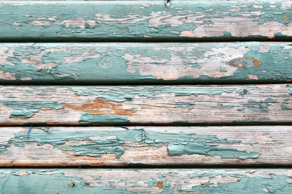Weathered wood boards with green paint peeling off in patches