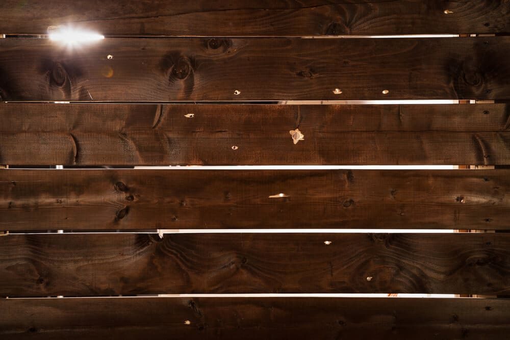 Dark wood fence boards with small holes and thin gaps that let light through