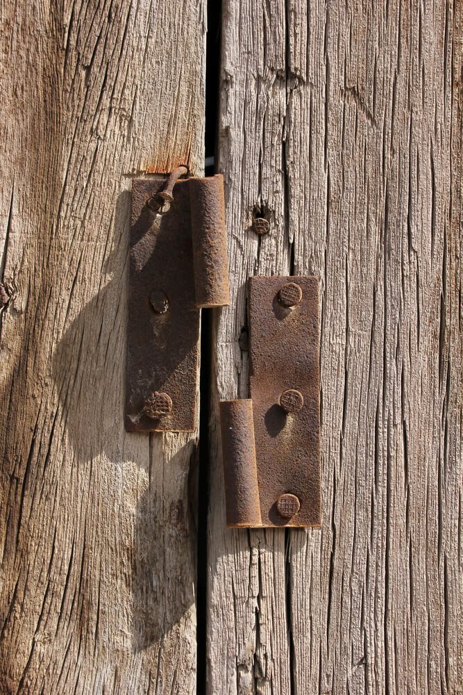 Rusty metal hinges screwed onto weathered wood boards