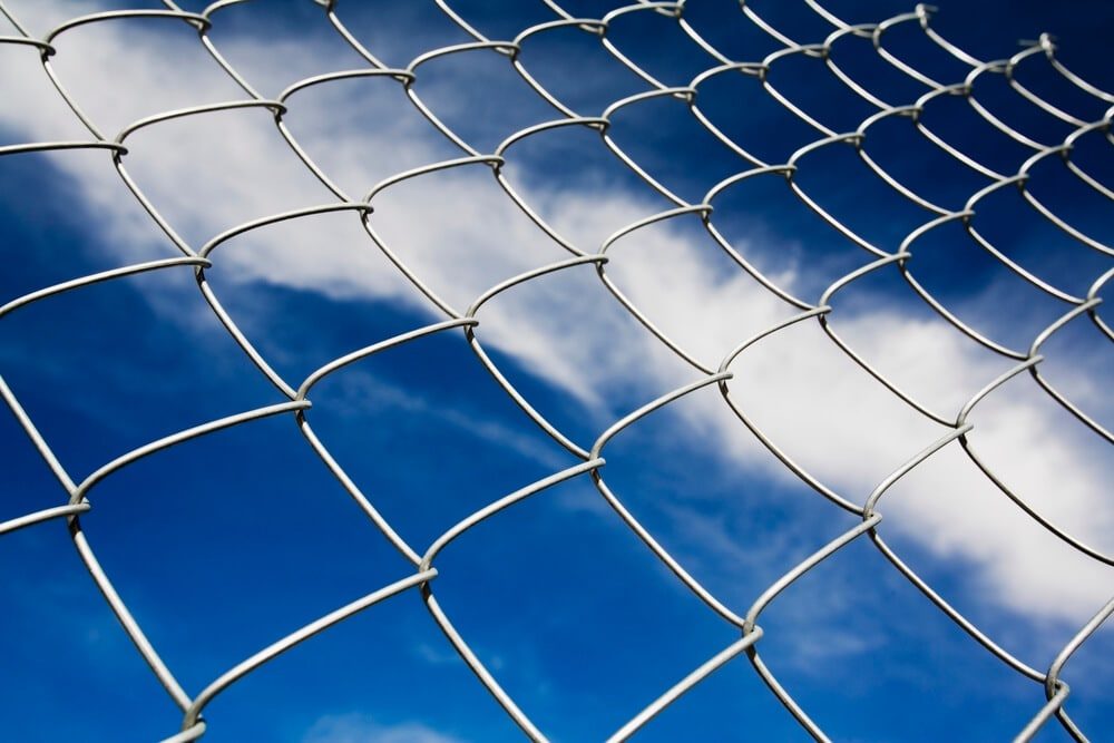 Close-up of galvanized chain link mesh against a blue sky