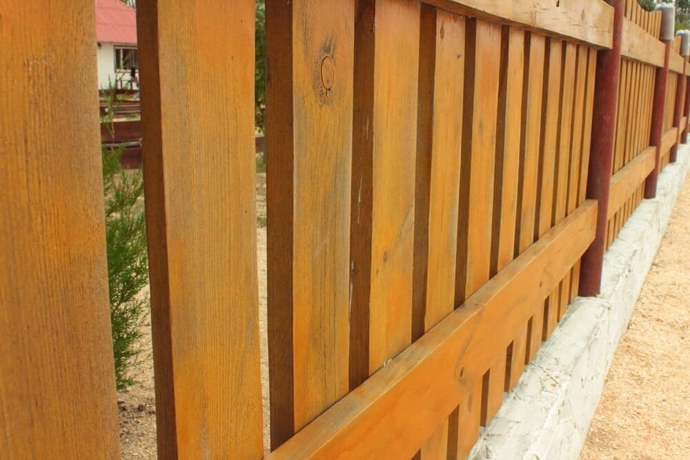 A stained wood fence with amber-toned vertical boards and horizontal rails on a concrete base