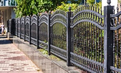 A black ornamental metal fence with arched tops running along a brick sidewalk