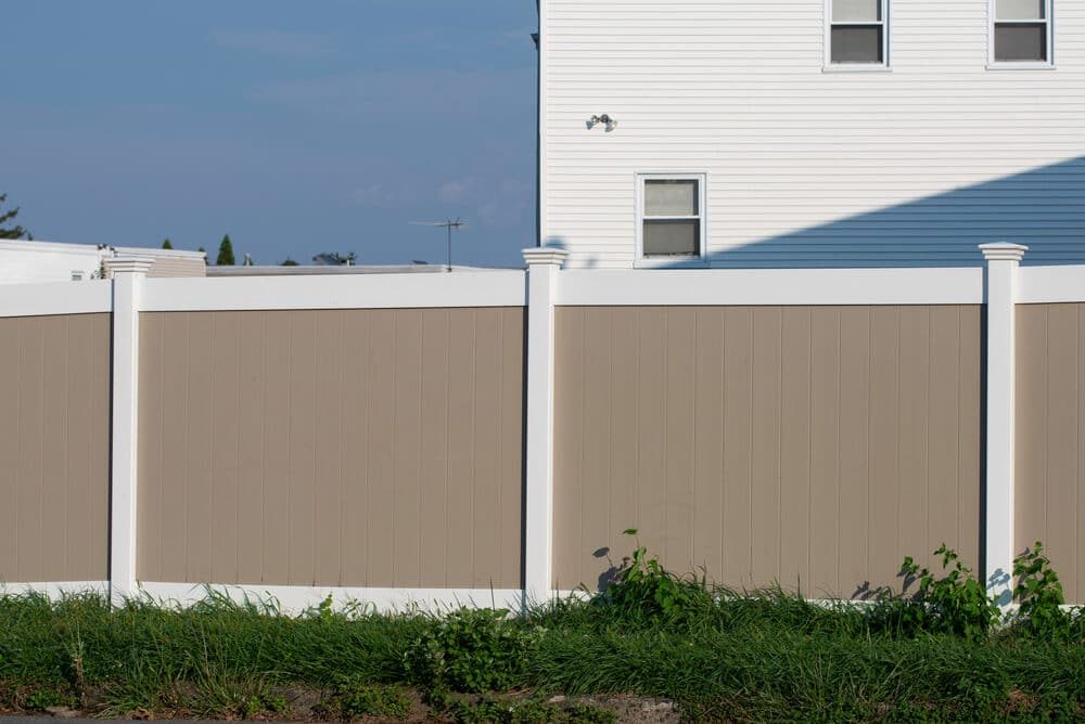 A two-tone tan and white vinyl privacy fence beside a white house