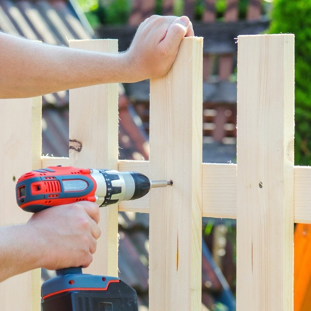 A person drilling a screw through a wood picket into a rail on a new fence