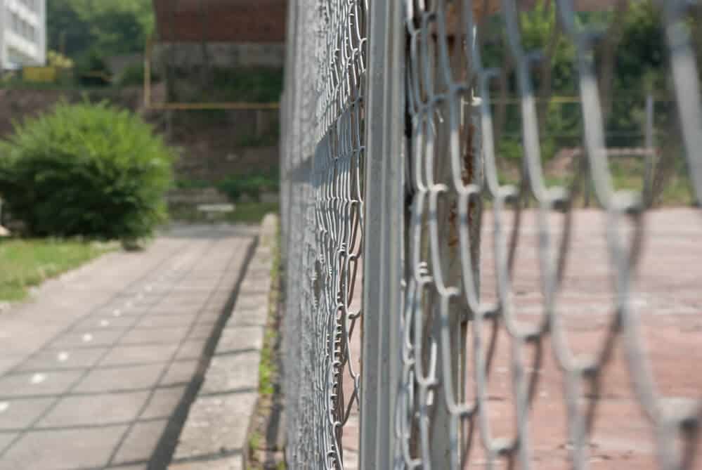 Close-up of a galvanized chain link fence running along a paved walkway
