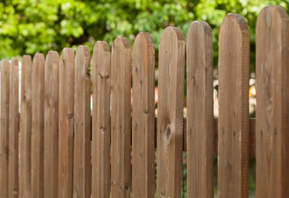 Close-up of brown wood pickets with rounded tops and visible grain and small knots