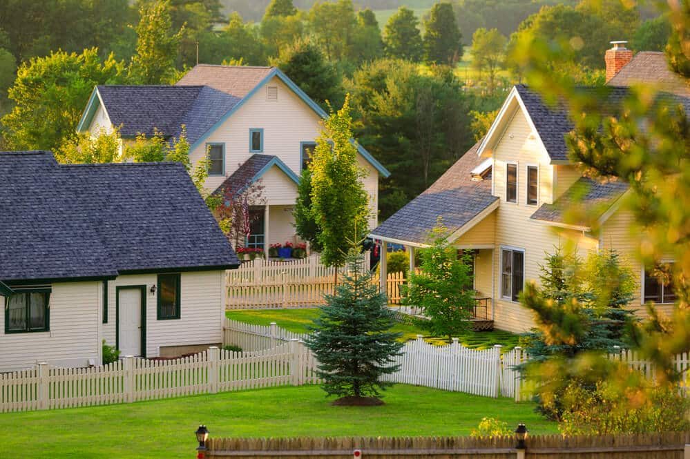 Houses in an evening-lit neighborhood with white picket fences around the yards